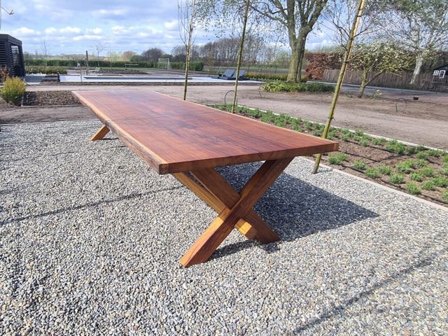 Lange massief houten tuintafel met houten X poten geplaatst in een landelijke tuin