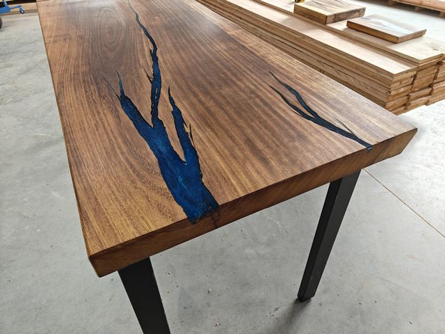 Massief houten tafelblad met natuurlijke scheuren gevuld met blauwe epoxy en zwart stalen poten