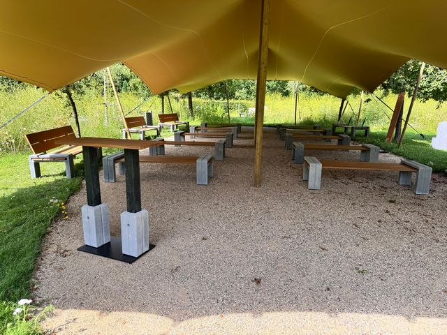 Buitenaula met maatwerk houten banken en spreektafel onder een grote overkapping