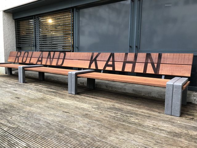 Lange houten maatwerk bank met betonnen poten en naam in de rugleuning