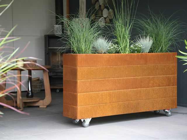Cortenstaal plantenbak op wielen met siergrassen op een overdekt terras