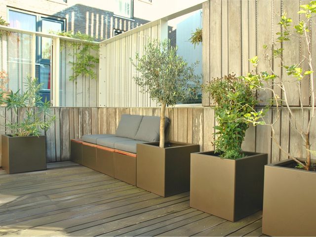 Stalen plantenbakken met bomen en houten zitbank op een modern dakterras