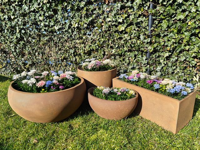 Ronde en rechthoekige corten plantenbakken met kleurrijke bloemen in de tuin