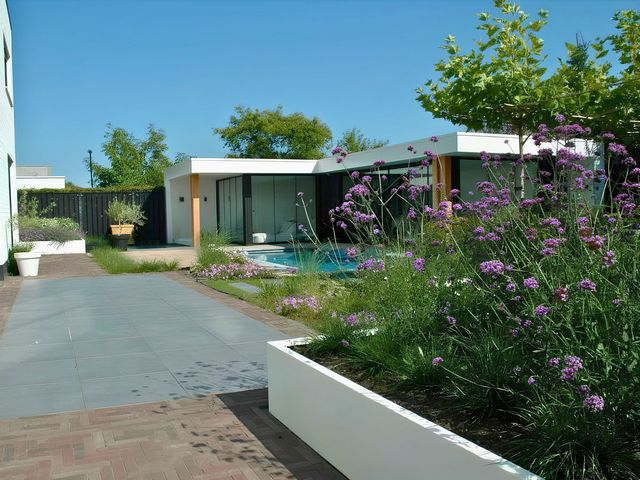 Lange witte stalen plantenbak met siergrassen en bloeiende beplanting in een moderne tuin