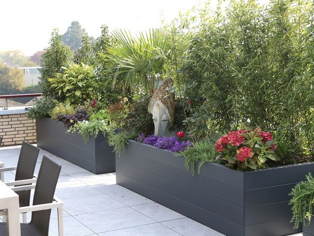 Grote antraciet stalen plantenbakken met bomen, bloemen en groene beplanting op een dakterras