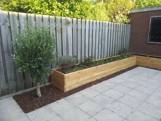 Lange houten plantenbak als verhoogde border met beplanting langs een schutting in de tuin