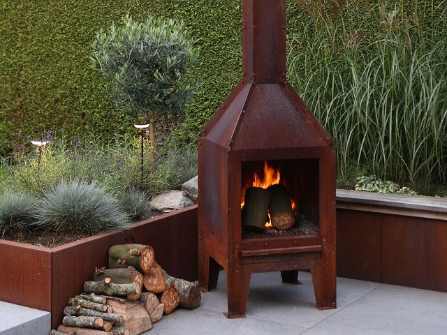 Cortenstalen buitenhaard met brandend hout tussen cortenstalen plantenbakken