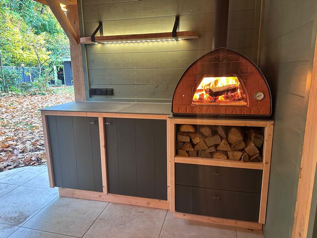 Houten buitenkeuken op maat met pizzaoven en opbergruimte onder een overkapping