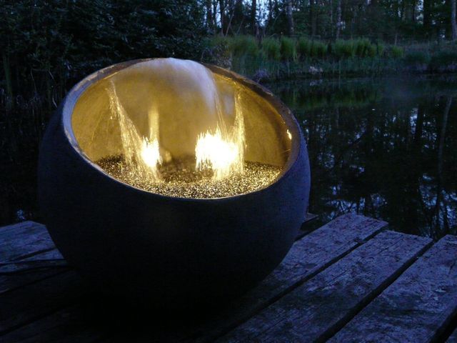 Rond waterornament met waterval en sfeerverlichting aan de rand van een vijver